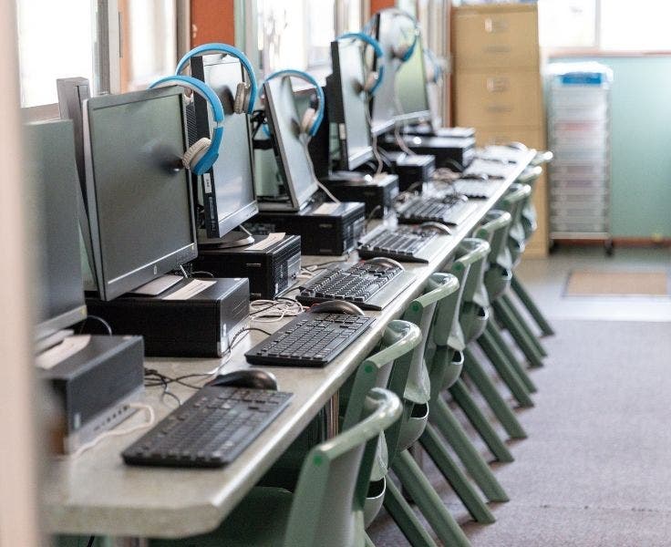 8 computers lined up against the wall of the bright classroom verandah.
