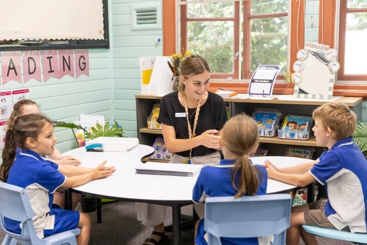 Teacher sitting at the jellybean desk teaching 4 students and using hand signals to break up the words they are learning.