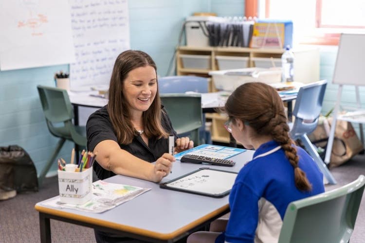 Teacher working one to one with student at their desk. Student and teacher are using a whiteboard and marker.