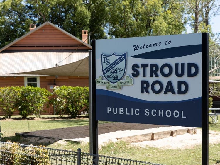 View of the school sign at the front of the school and the classroom building and sandpit are in the background