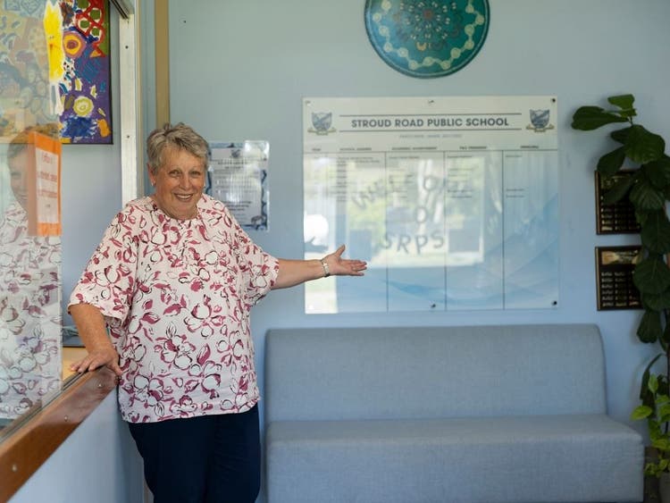 The SAM stands in the office area holding her hand out in welcome. The honour board is on the far wall, with a small lounge sitting underneath.