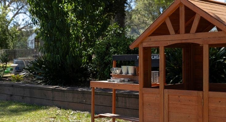 Cubby house and mud kitchen sit the foreground on the right and the gardens are in the background to the left.